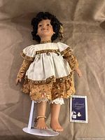 Full view of doll lying flat showing dress, feet, stand, booklet