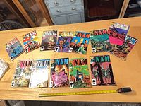 Wide shot of thirteen The 'Nam comics laid out on table with tape measure for scale