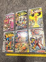 Six consecutive Uncanny X-Men comics issues 122-127 laid out in two rows with measuring tape for scale