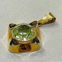 Front view of gold pendant showing square openwork setting and round pale green gemstone