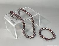 Necklace draped over clear stand with bracelet beside