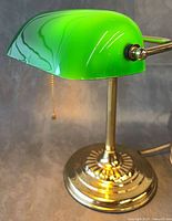 Full view of lamp illuminated showing brass base, green glass shade, pull chain