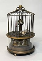 Front view showing full birdcage clock with rotating numeral drum and bird