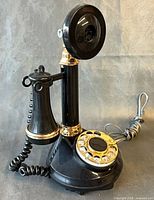 Front view of black and gold candlestick rotary telephone showing handset, mouthpiece, and coiled cord