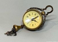 Full view of brass-tone OMEGA pocket watch lying on side with attached bell fob and chain