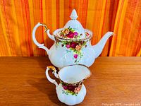 Teapot with lid and matching creamer pitcher on wood surface