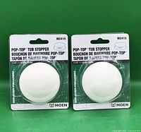 Front view showing both packaged Moen Pop-Top tub stoppers