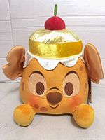 Front view of Disney Munchlings Pineapple Upside-Down Cake plush showing face, feet, cherry topper, tag visible