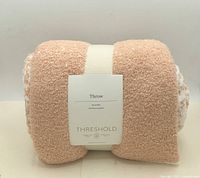 Front view of rolled peach and white Threshold throw with front label