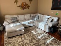 Full view of assembled four-piece beige sectional with chaise and throw pillows on patterned rug
