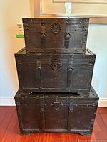 Three stacked dark brown plywood trunks with metal hardware and faux leather straps