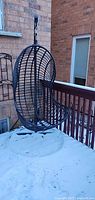 Full view of hanging egg chair suspended from stand on snowy deck