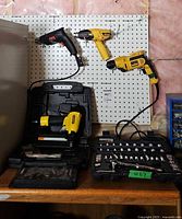Overall lot showing three handheld tools on pegboard, nailer in case, socket set