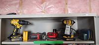 Shelf holding DeWalt drill, loose battery, Milwaukee Hackzall, charger, DeWalt impact driver, soft case