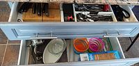 Open kitchen drawers showing cutlery, knives, utensils, measuring cups, CorningWare dish, juicers, Ziploc box