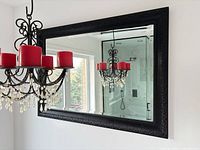 Framed wall mirror hanging above chandelier, shows full frame and reflection