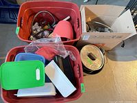 Overview of two red bins and cardboard box containing plastic containers, lids, pots, cords, and utensils