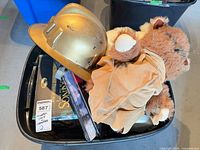 Bin containing gold decorative helmet, plush stuffed animal, books and assorted items