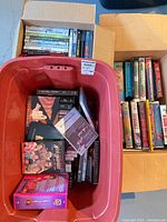 Red tote with numerous DVD and Blu-ray cases; adjacent box of VHS tapes; small box of additional discs