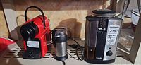 Red Breville Nespresso machine, stainless Breville grinder, small stainless accessory on shelf