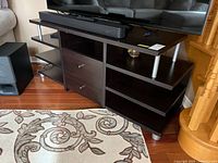 Front view of dark espresso laminate TV stand with raised shelf, drawers, side shelves, and metal supports