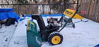 Side view of Yard-Man two-stage gas snowblower on snow showing green auger housing, engine, yellow wheel rims