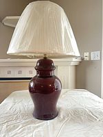 Full view of table lamp showing burgundy ceramic base and pleated cream shade wrapped in plastic