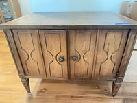 Front view of medium brown wood console table cabinet with two paneled doors and metal knobs