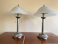 Pair of brushed nickel table lamps with frosted glass shades shown side by side on wooden surface