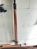 Six wooden poles leaning against wall, showing full length and baskets