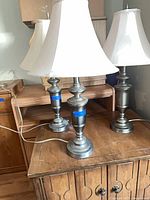 Three metal table lamps with shades on wooden furniture