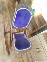 Three-quarter view of chair showing purple velvet upholstery and carved crest