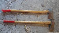 Two large single-bit axes lying side by side showing full length handles and heads