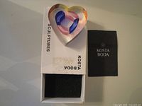 Heart glass sculpture beside original box and booklet