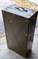 Front view of tall riveted olive drab metal trunk with handle and reinforced corners