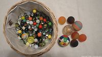 Basket filled with assorted marbles with rubber balls alongside