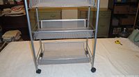 Front view of metal mesh utility cart showing three baskets and casters