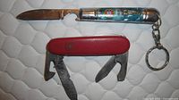 Two pocket knives, one red Swiss Army, one blue souvenir with keyring