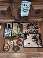 Drawer view showing needlepoint medallions, postcards, straw ornament, framed cross-stitch and one silhouette panel