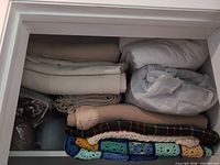 Closet shelf with stacked blankets and throws, showing variety of items