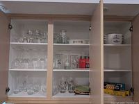 cabinet shelves showing assorted clear stemware, boxed tea glass set, plates, foil and wrap