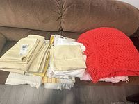 Folded cream sheets, assorted sheets and coral knit throw on couch