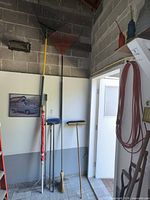 corner view showing two leaf rakes, umbrella, push broom, corn broom, squeegee
