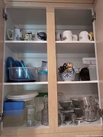Cabinet view showing mugs, storage containers, bowls, decanter, egg cups