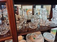 Cabinet shelf with multiple clear lead crystal items including vases, bowls, boxes, mug, cruet