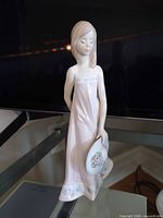 Front view of Lladro Girl with Hat figurine standing on glass shelf