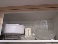 Shelf view with milk glass bowl on rectangular dish, small pressed glass dish, speckled mug, clear etched punch bowl