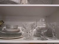 Shelf with pressed glass goblets, balloon wine glass, stacks of plates