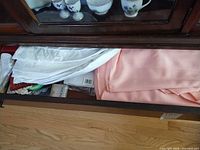 Drawer view showing packaged white napkins, pink tablecloth, Oneida box, fragment of lace doily
