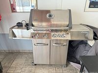 Front view of Napoleon Prestige 500RB stainless steel propane grill showing four control knobs, cabinet, side shelves and lid thermometer